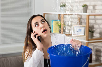 woman with bucket of water under leaking ceiling 